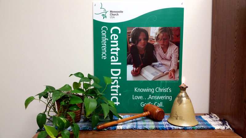 A Central District Conference promotional sign, a gavel, and a monogrammed oil lamp sitting on a table